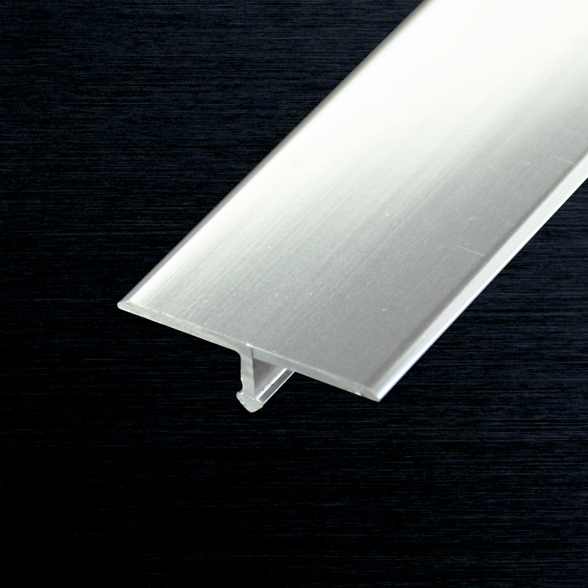 A brushed T-profile trim piece shown diagonally against a dark textured background.