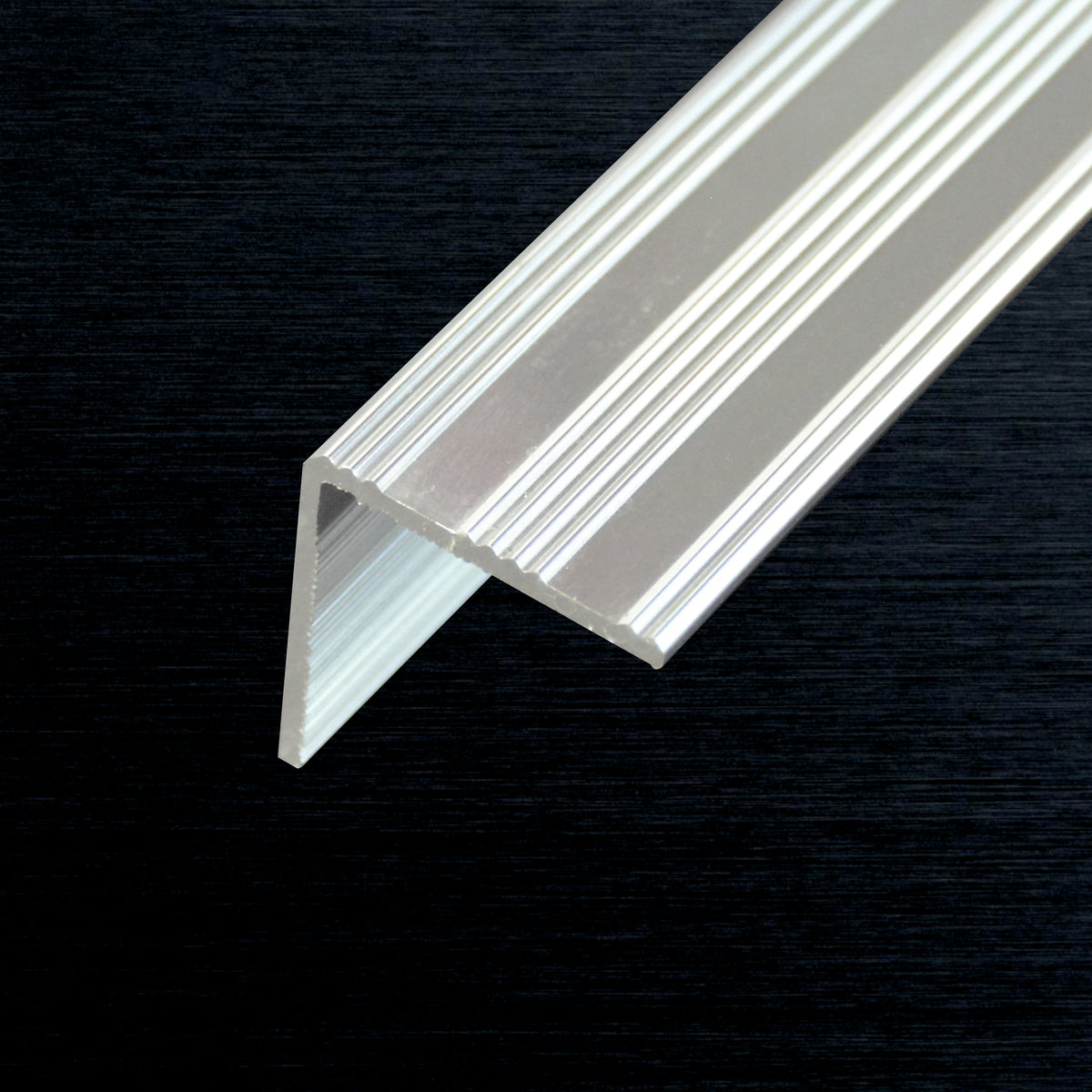 A close-up of a line edge angle profile piece with a ribbed surface, shown against a dark textured background.