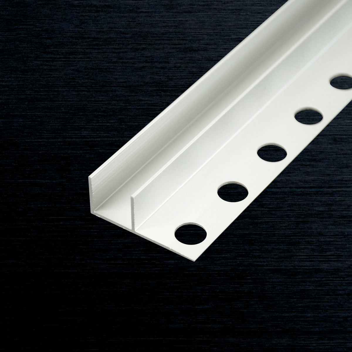 A white metal F-shaped architectural trim with four circular mounting holes, shown diagonally on a dark textured background.
