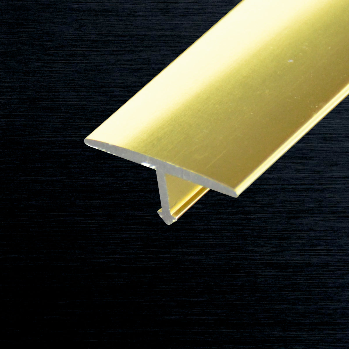 A close-up of a metallic gold T-profile piece on a dark textured background.