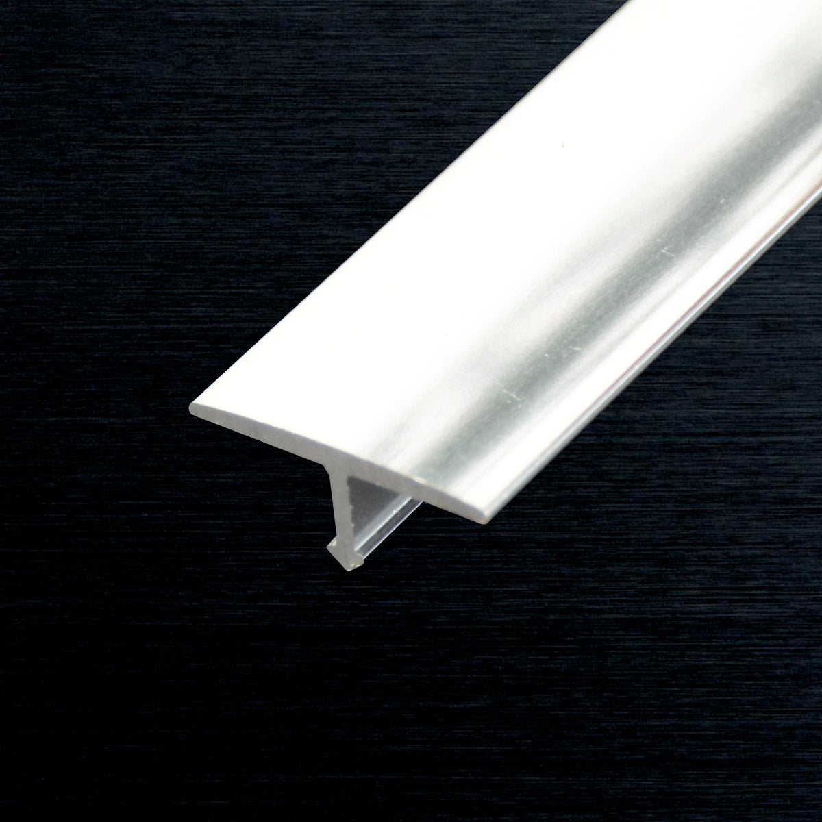 A long, narrow silver metal  T-profile piece shown diagonally against a dark textured background.