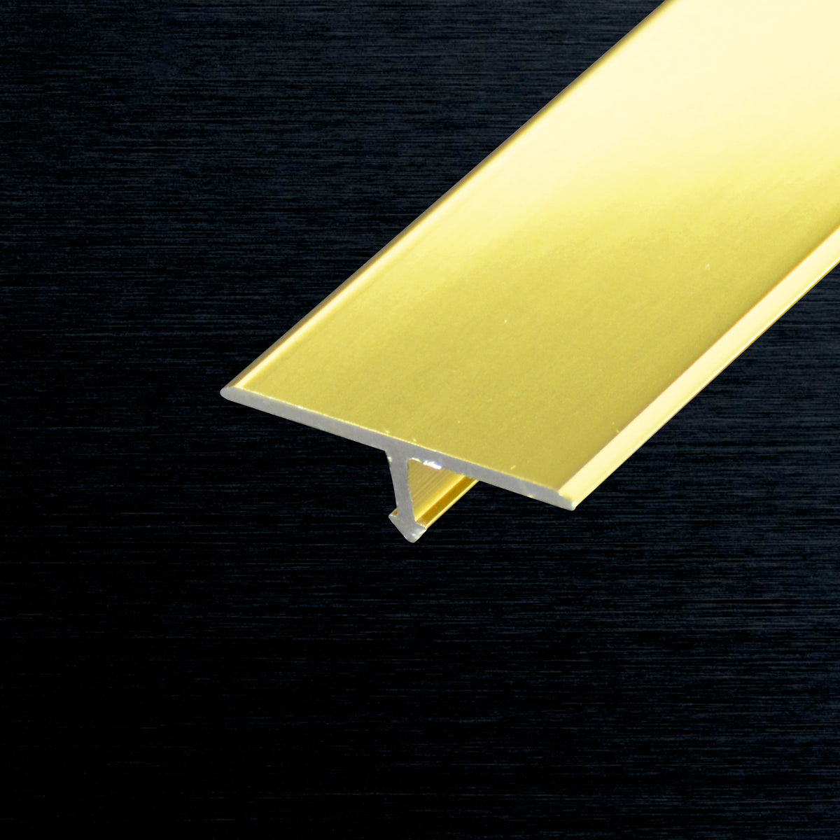 A close-up of a metallic gold aluminum T-profile cross-section, shown against a dark textured background.