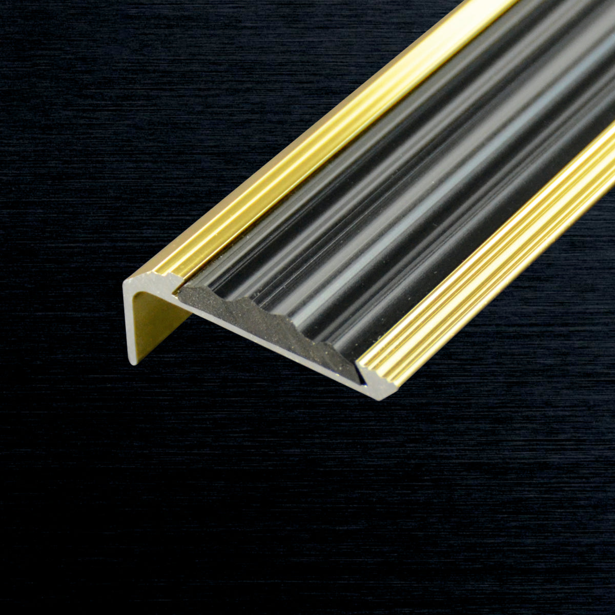 Gold aluminum stair nosing profile with a ribbed translucent gray center, shown in a close-up diagonal view against a dark textured background.