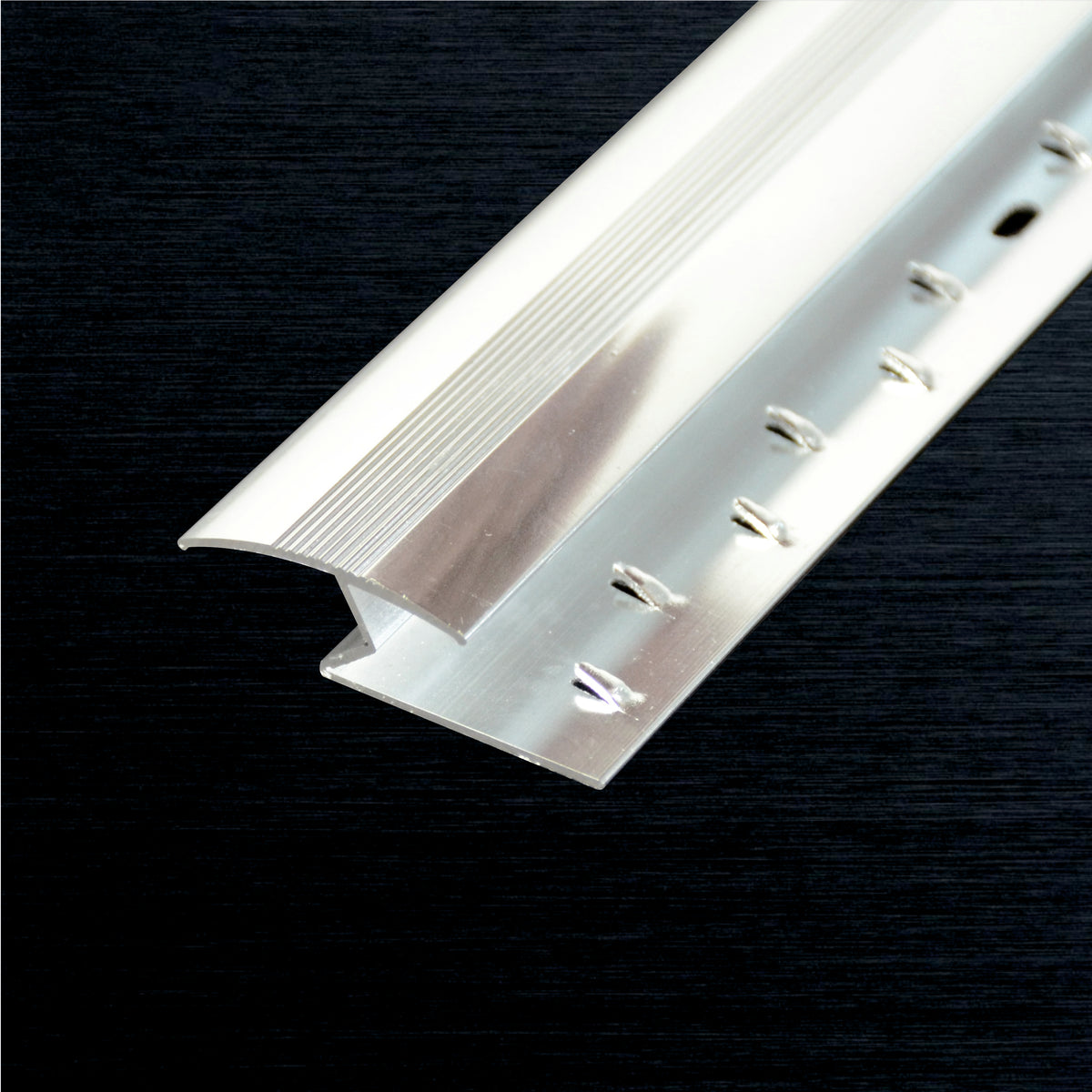 A close-up of a silver aluminum Z-profile with a ribbed top surface and pre-drilled holes along one side, shown diagonally against a dark textured background.