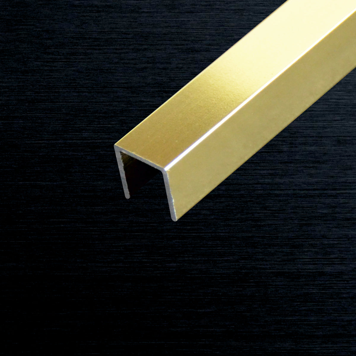 A close-up of a polished gold U-shaped metal channel bar resting diagonally on a dark, textured black background.