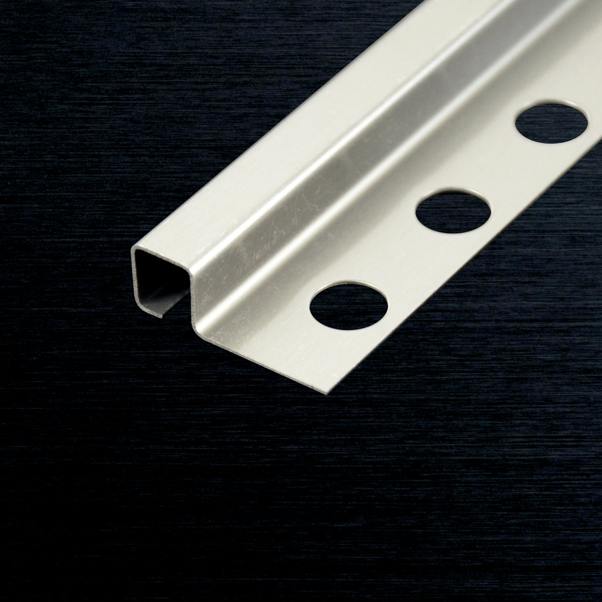 A silver tile corner profile with three pre-drilled circular holes, shown diagonally on a dark textured background.