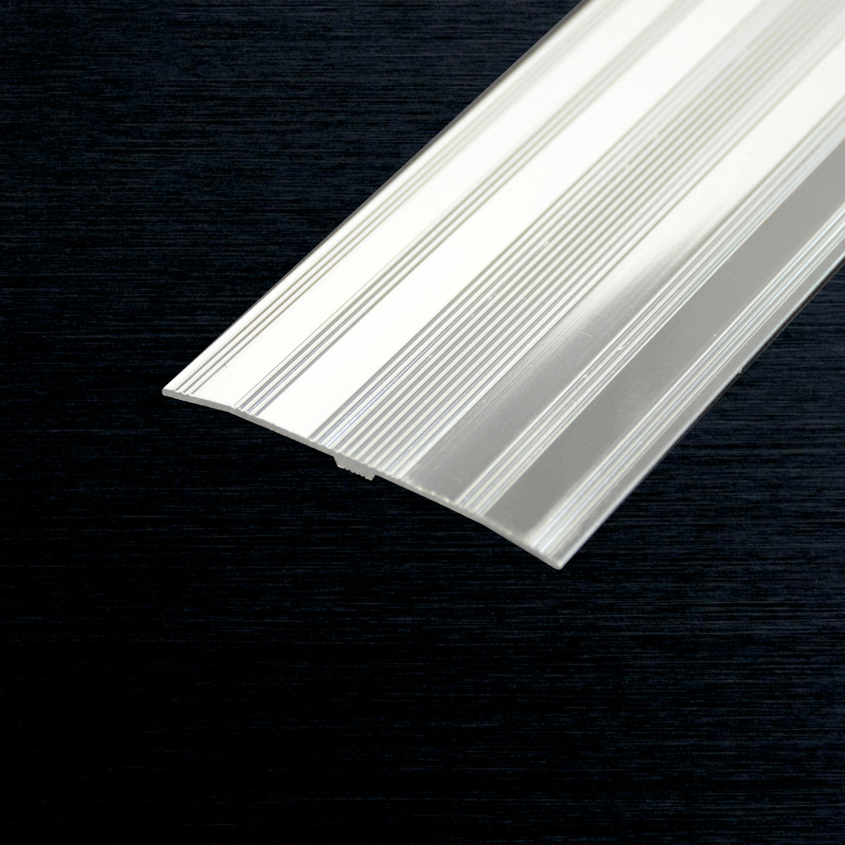 A close-up of a translucent white ribbed cover strip piece shown diagonally against a dark textured background.