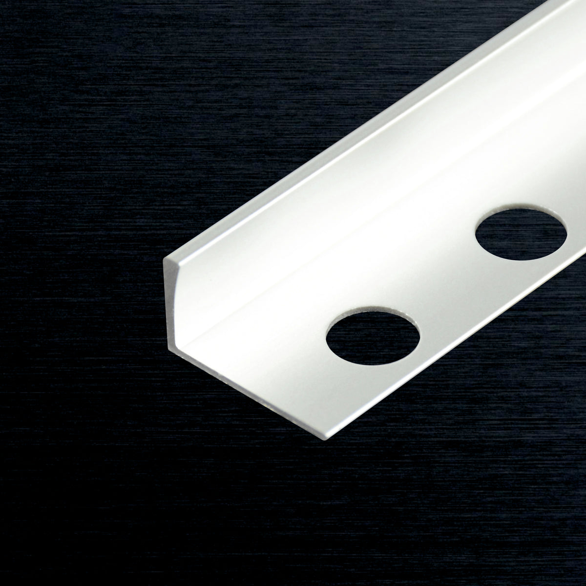 A close-up of a silver metal L-profile with two circular holes, shown diagonally on a dark textured background.