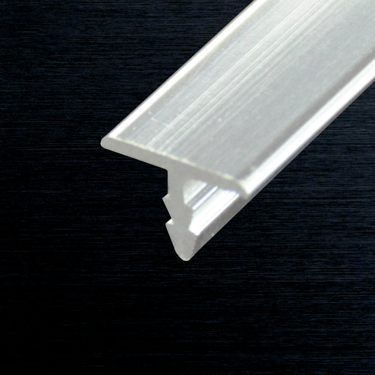 A close-up of a clear T-profile piece with a recessed channel, shown diagonally against a dark textured background.