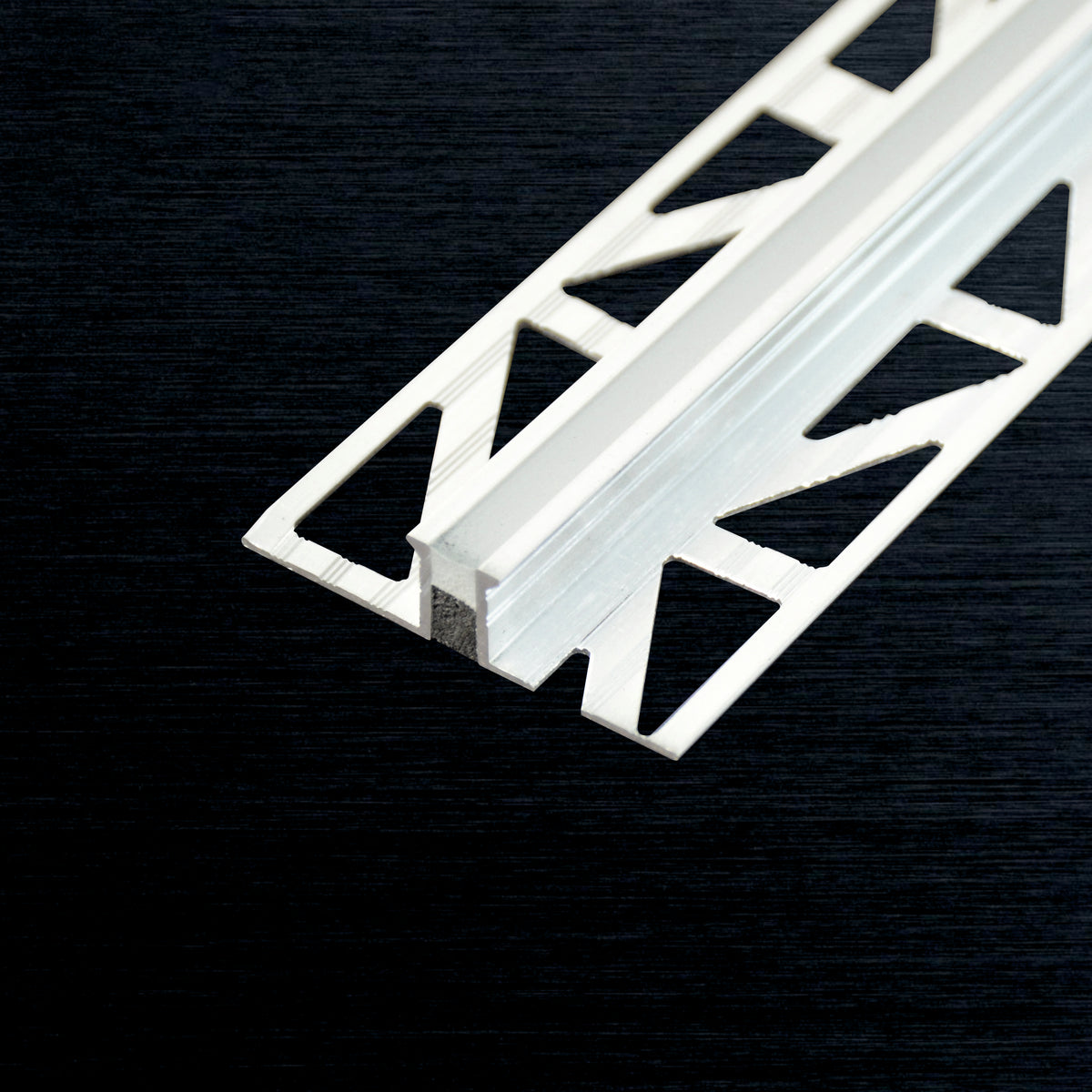 White aluminum expansion joint profile with triangular cutouts, shown diagonally on a dark textured background.