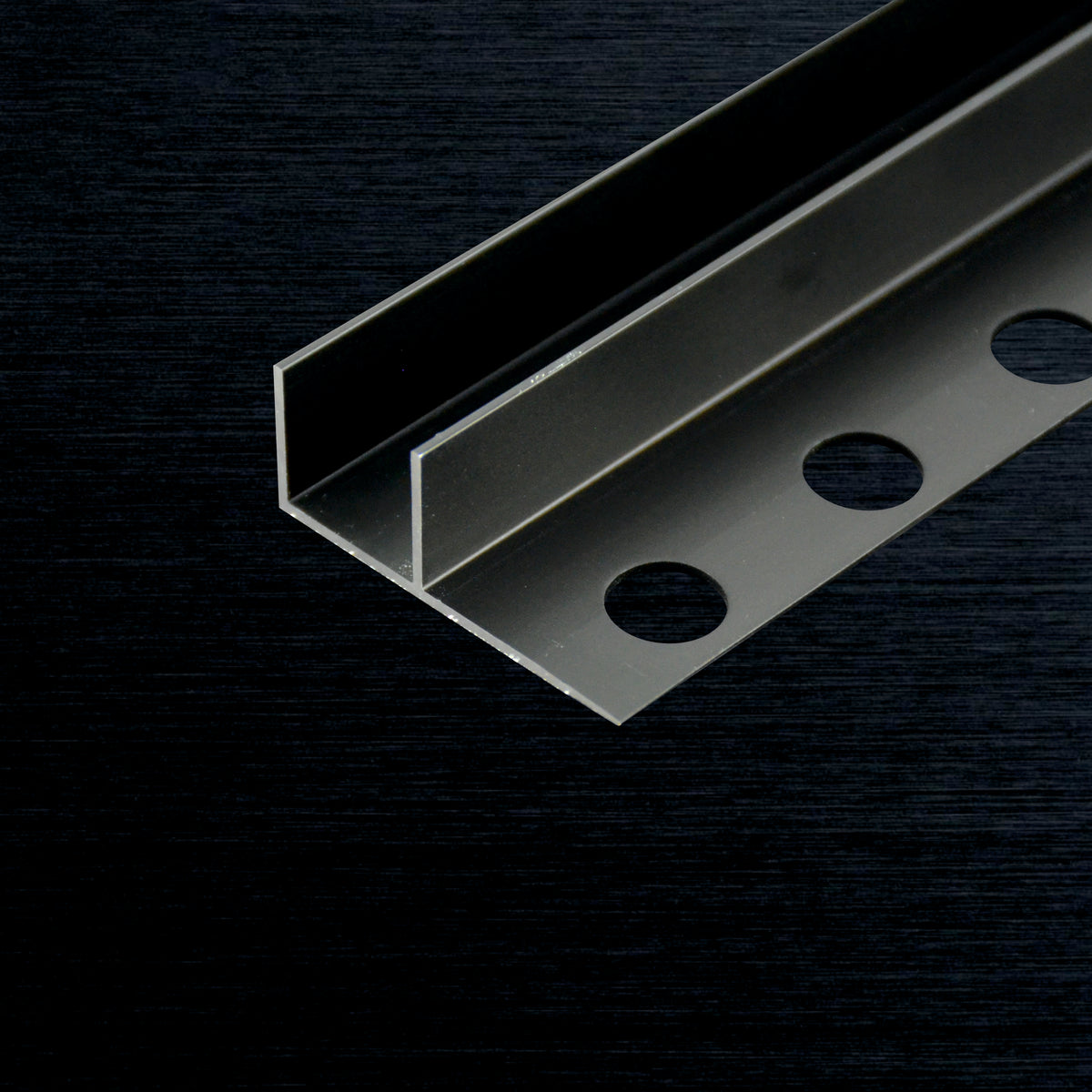 A close-up of a metallic F-Profile with three pre-drilled circular holes, shown on a dark textured background.